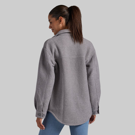 A woman is shown from the back wearing a heather gray button-up jacket and blue jeans against a solid gray background.