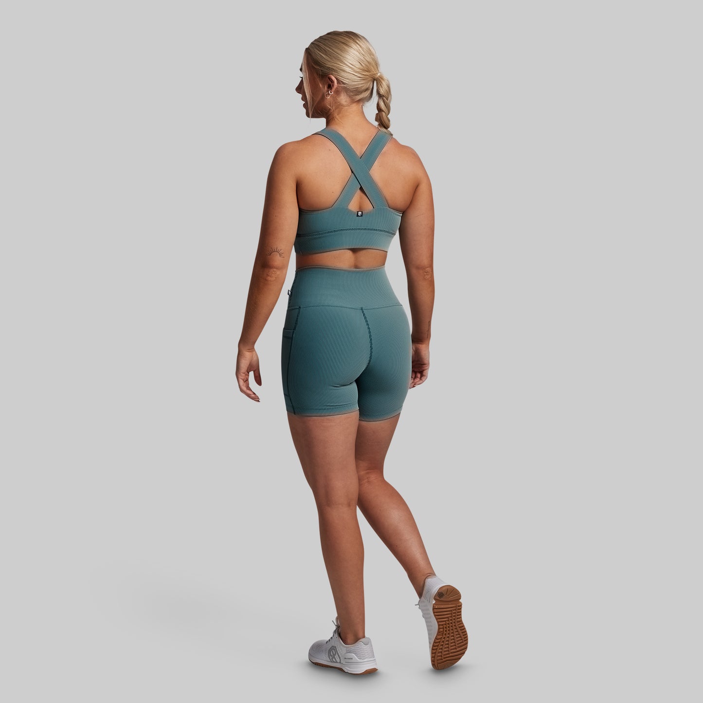 Woman wearing a green sports bra and shorts set on a gray background
