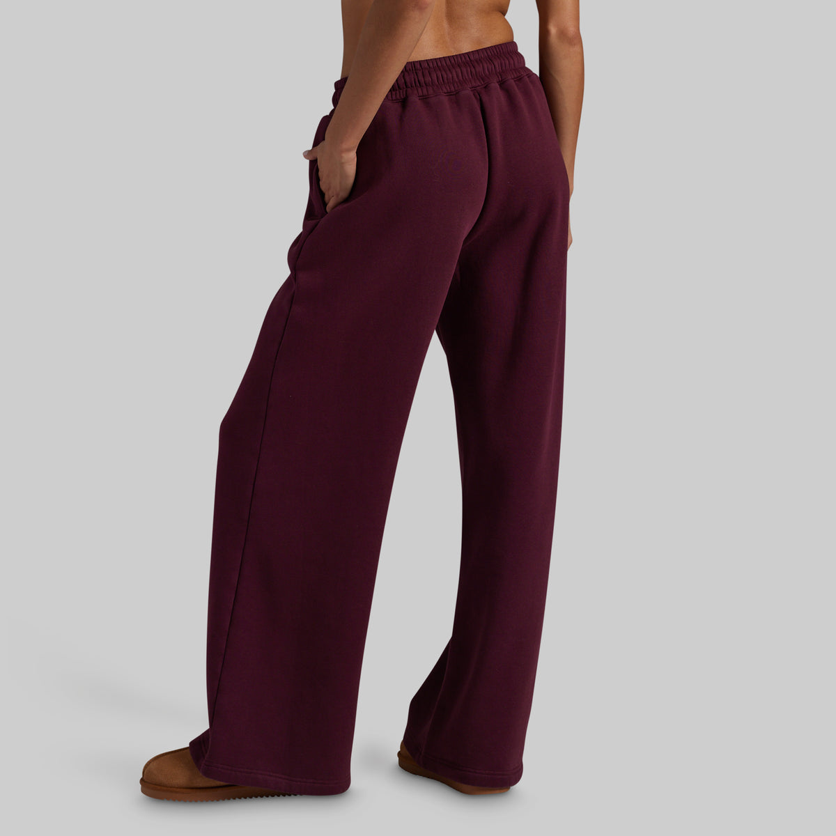 A model wearing wide-leg lounge pants in deep burgundy, paired with brown suede slippers, shown from behind.