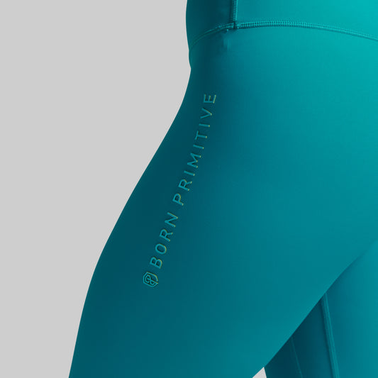 Teal leggings with 'Born Primitive' branding on a gray background