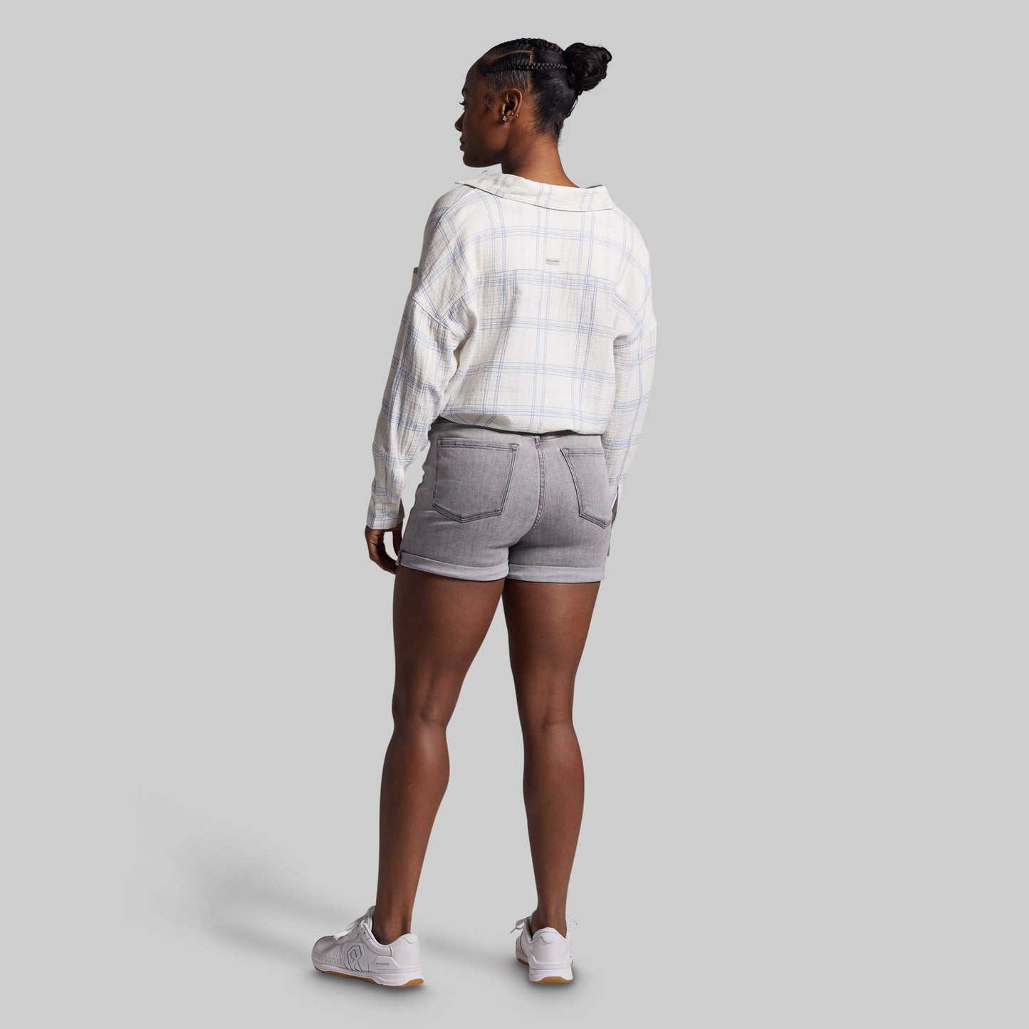 Person wearing a white plaid shirt and gray shorts on a light gray background