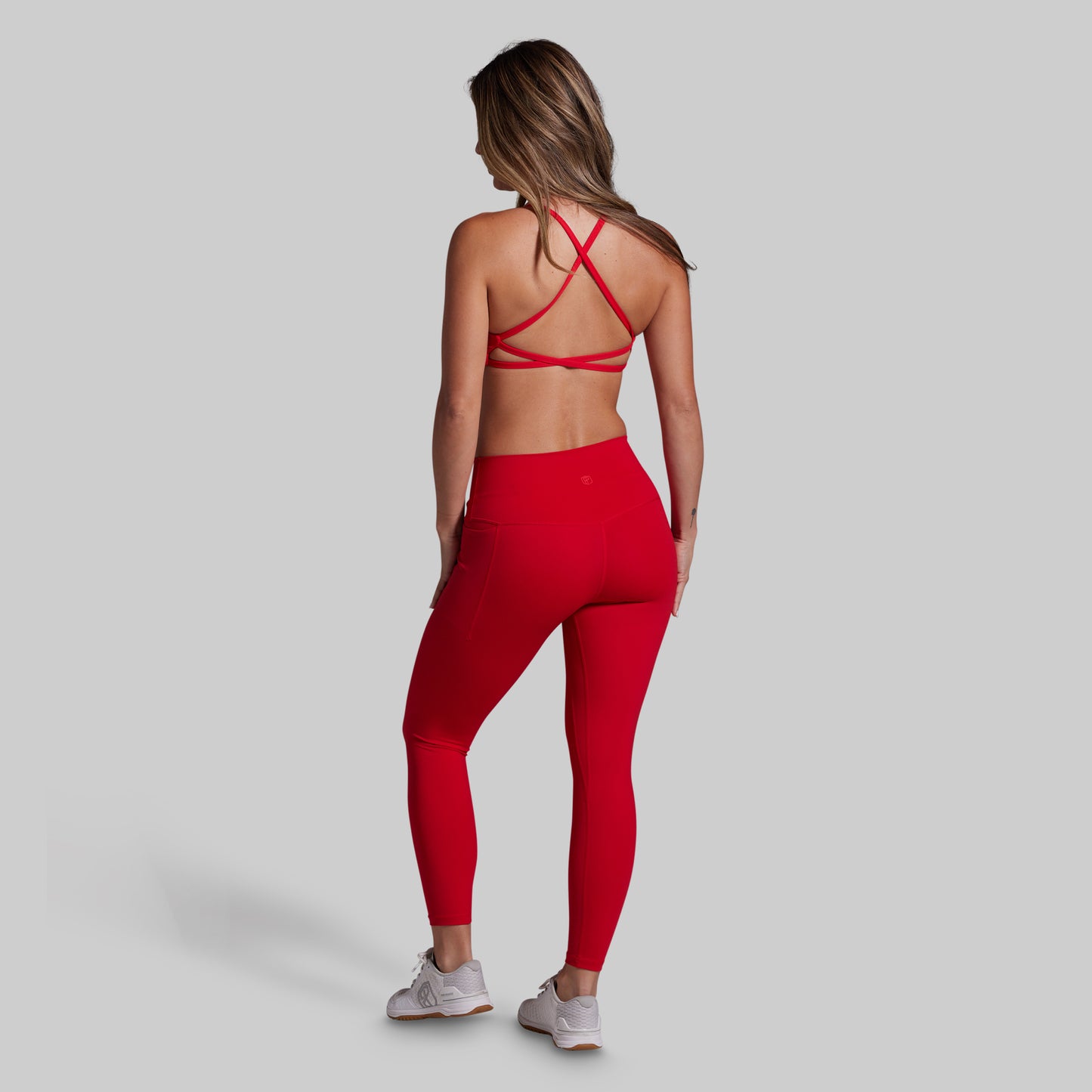 Woman wearing a red sports bra and leggings set on a gray background