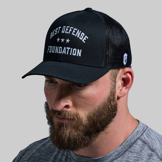 A man wearing a black trucker hat with 'BEST DEFENSE FOUNDATION' text on the front.