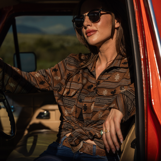 Woman wearing sunglasses and a patterned shirt sitting in a vehicle with a scenic background