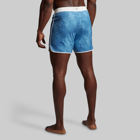 Blue swim shorts with white waistband worn by a person on a gray background