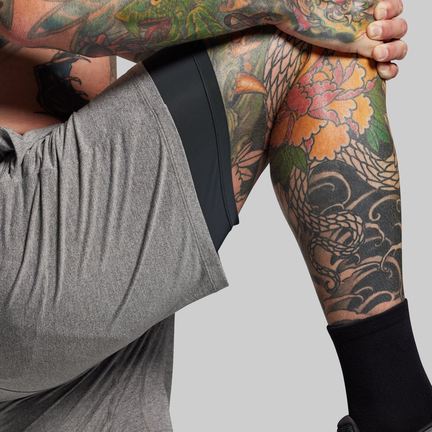 Person wearing gray shorts with black liner with colorful tattoos on a plain background