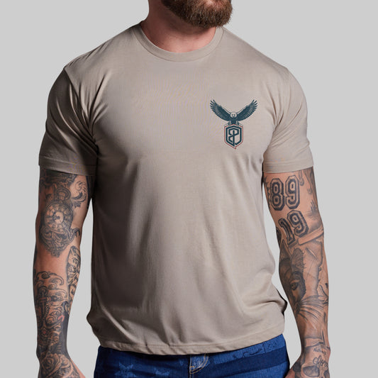 Man wearing a beige t-shirt with an eagle logo on a plain background