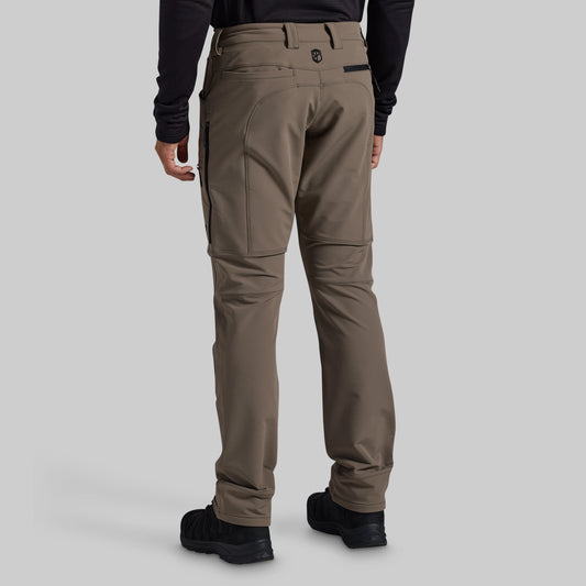 Rear view of a person wearing grey technical cargo pants with black boots and a black long-sleeve top, shown against a light gray studio background.