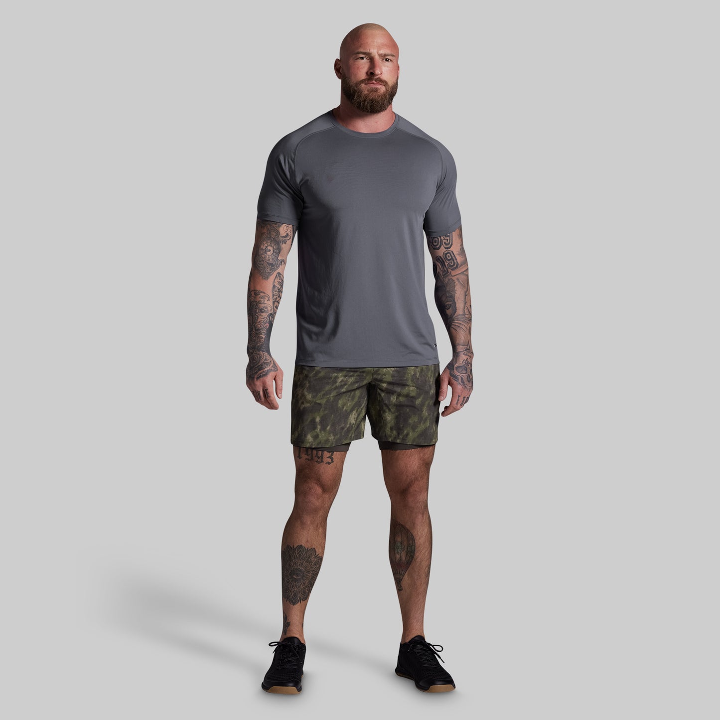 Man wearing a gray t-shirt and camouflage shorts on a plain background