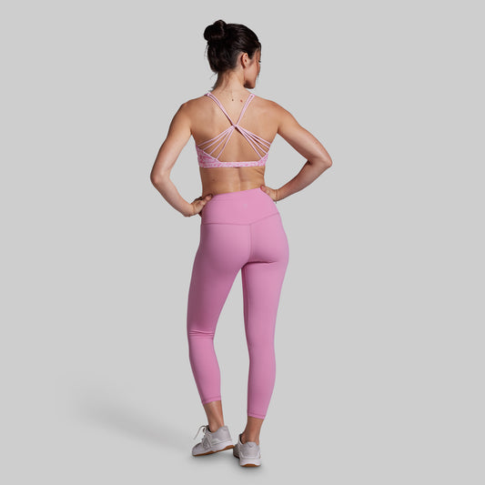 Woman wearing a pink sports bra and leggings set on a light gray background