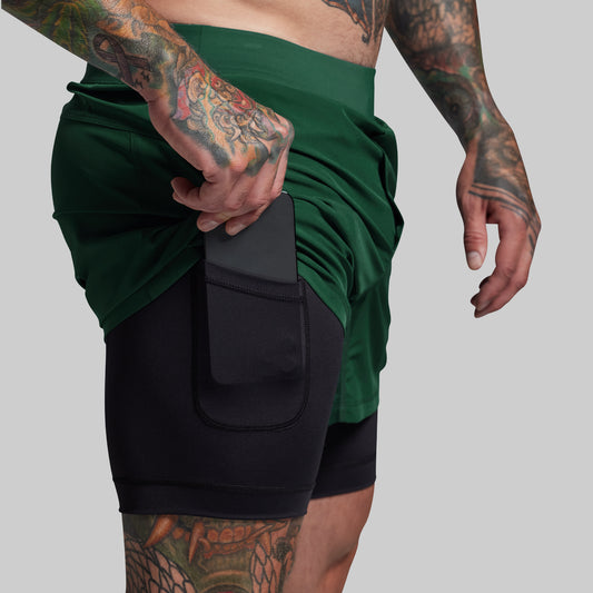 Person wearing a green shorts with black liner with a pocket on a gray background