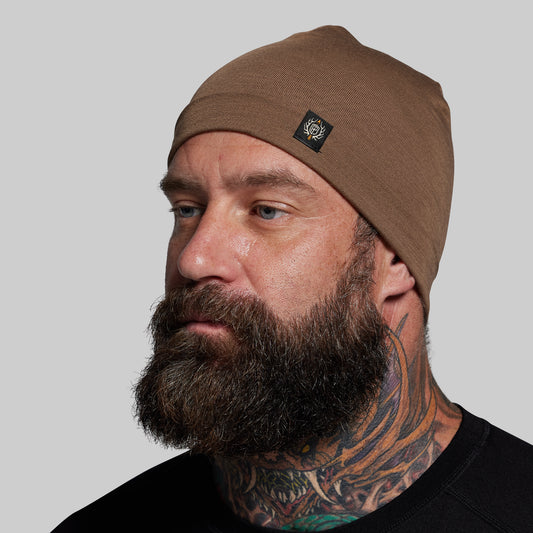 Man wearing a brown beanie with a logo on a gray background