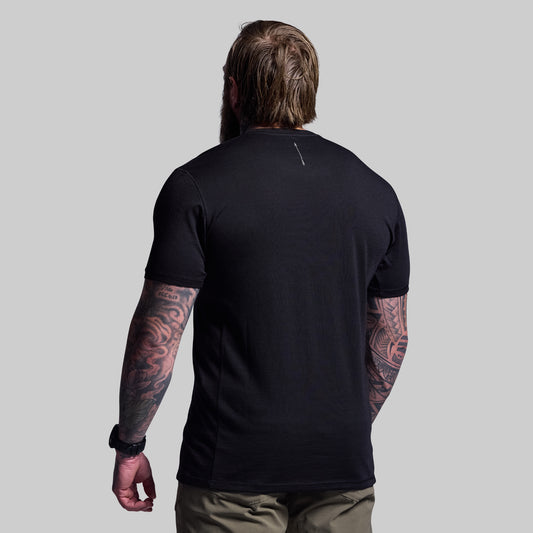 Person wearing a black t-shirt with visible tattoos on arms against a gray background