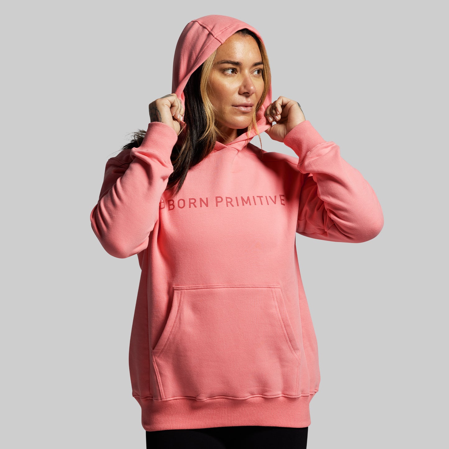 Person wearing a pink hoodie with 'BORN PRIMITIVE' text on a gray background