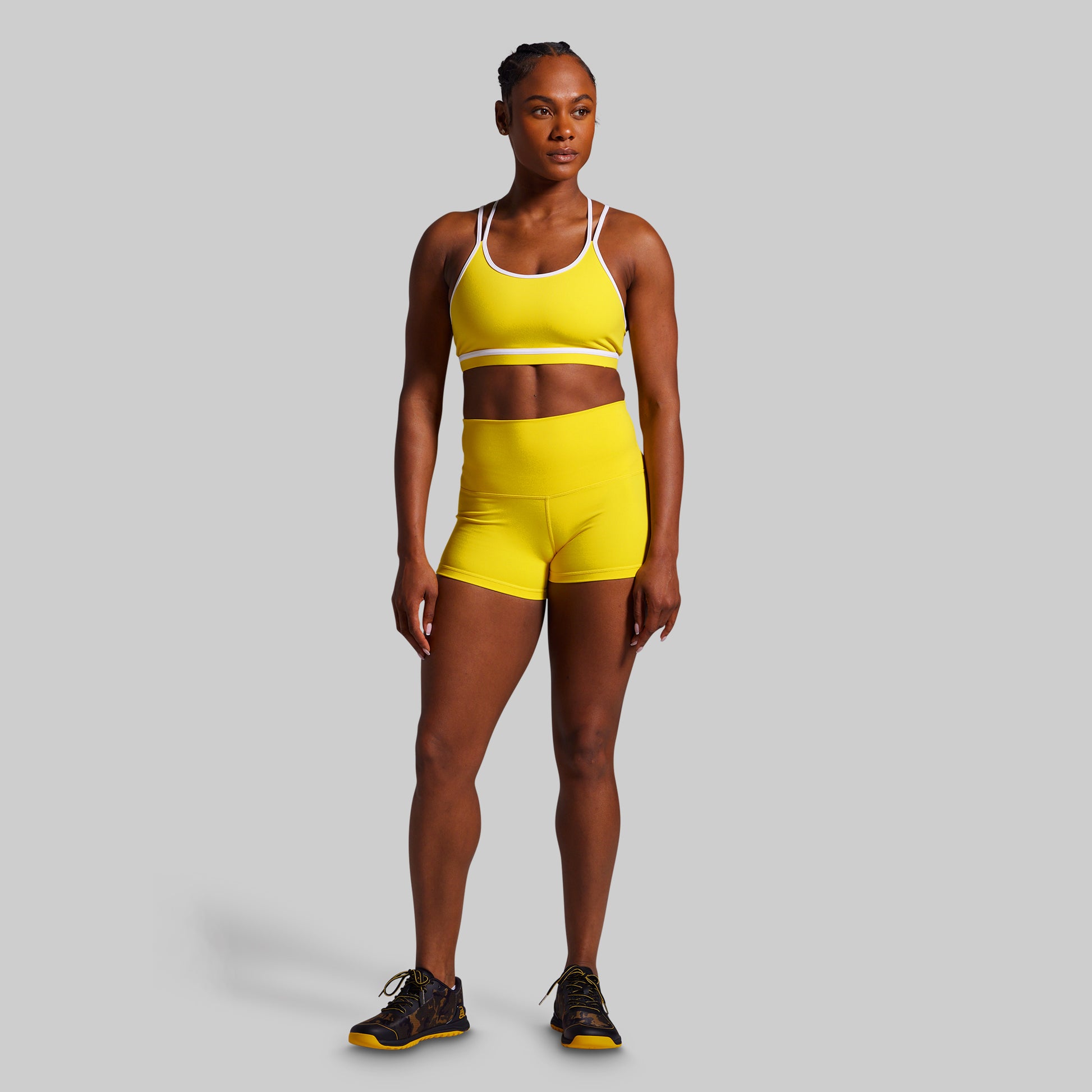 Woman wearing a yellow sports bra and shorts set on a gray background