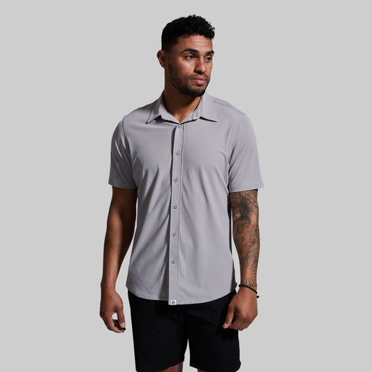A man wearing a short sleeve button-down shirt in gray color, paired with black shorts.