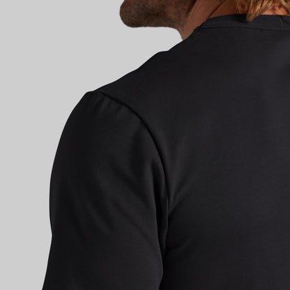 Close-up back view of a person wearing a plain black short-sleeve top against a light gray studio background.