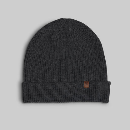 A dark charcoal gray ribbed knit beanie hat with a folded cuff and a small brown leather logo patch on the side, shown against a solid light gray background.