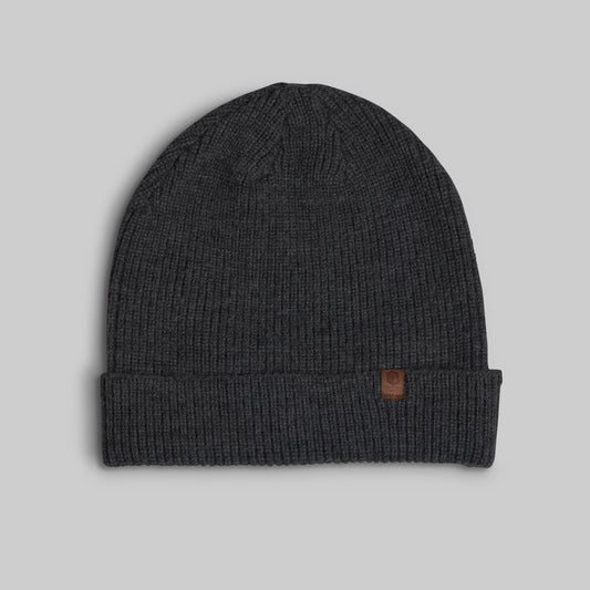 A dark charcoal gray ribbed knit beanie hat with a folded cuff and a small brown leather logo patch on the side, shown against a solid light gray background.