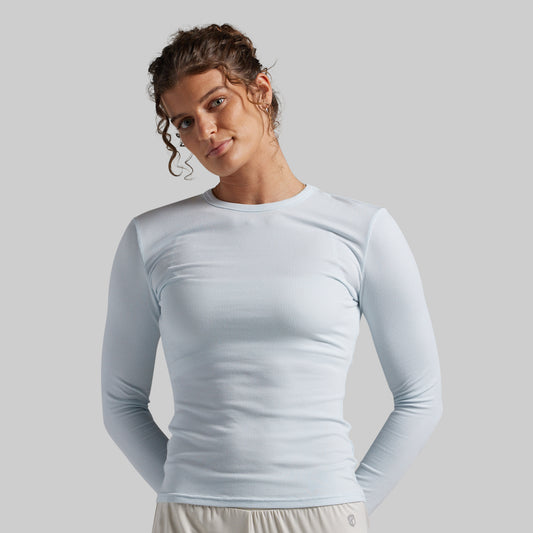 A woman wearing a light blue long-sleeve crewneck athletic top, photographed against a solid light gray background.