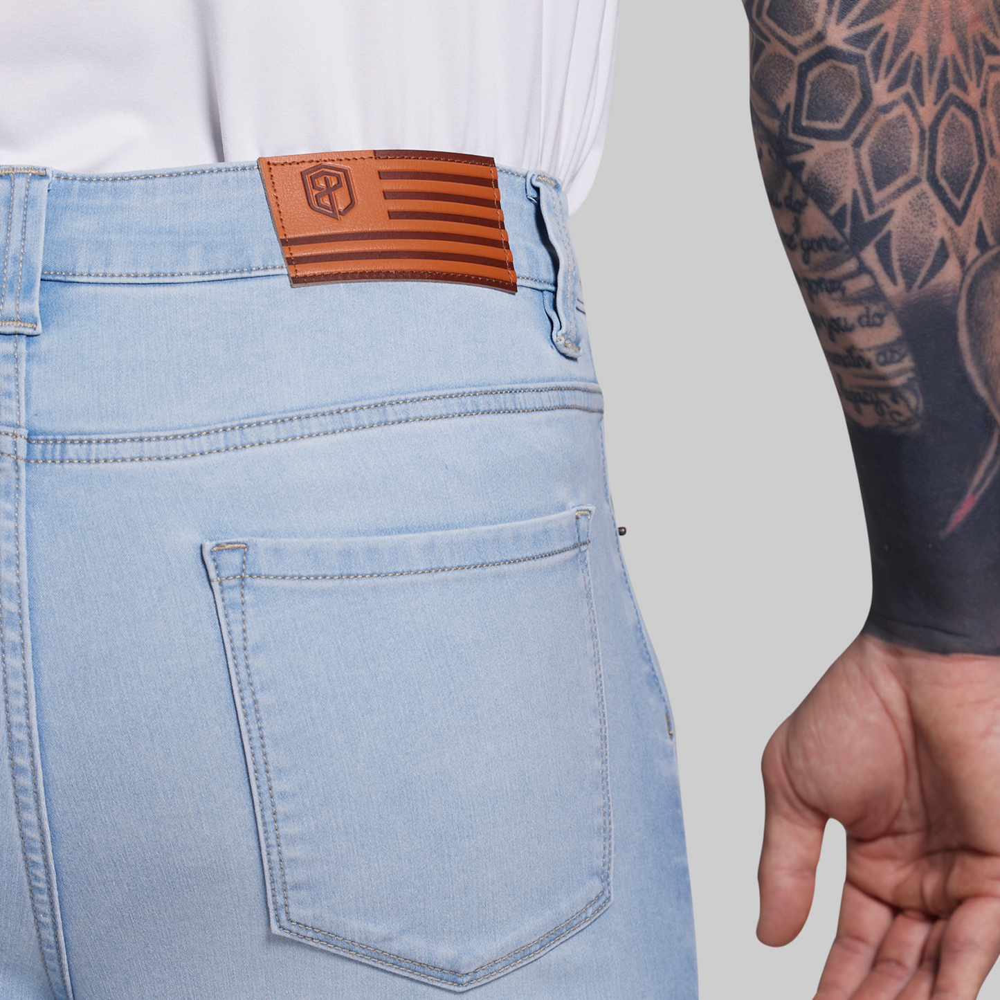 Light blue jeans with a brown leather patch on the back pocket, worn by a person with tattoos.