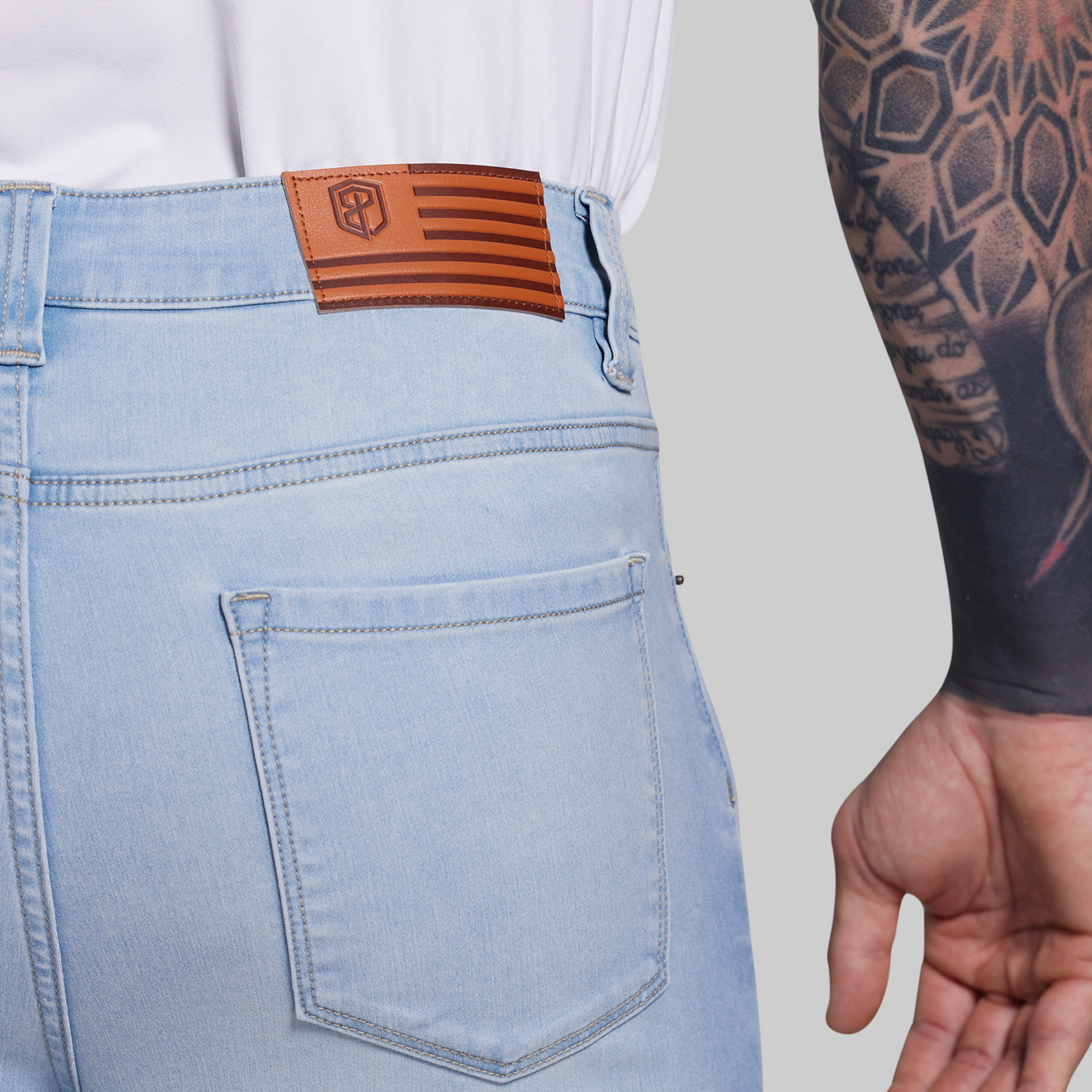 Light blue jeans with a brown leather patch on the back pocket, worn by a person with tattoos.