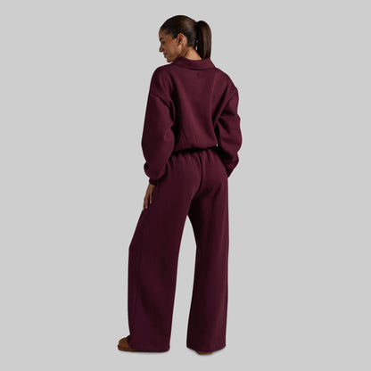A model shown from the back wearing a matching deep burgundy two-piece lounge set consisting of a cropped long-sleeve top and wide-leg pants, set against a solid light gray background.