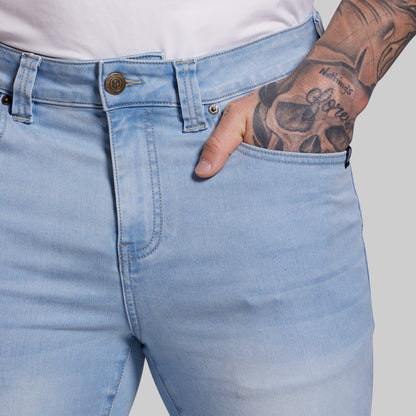 Light blue jeans worn by a person with a tattooed arm on a plain background