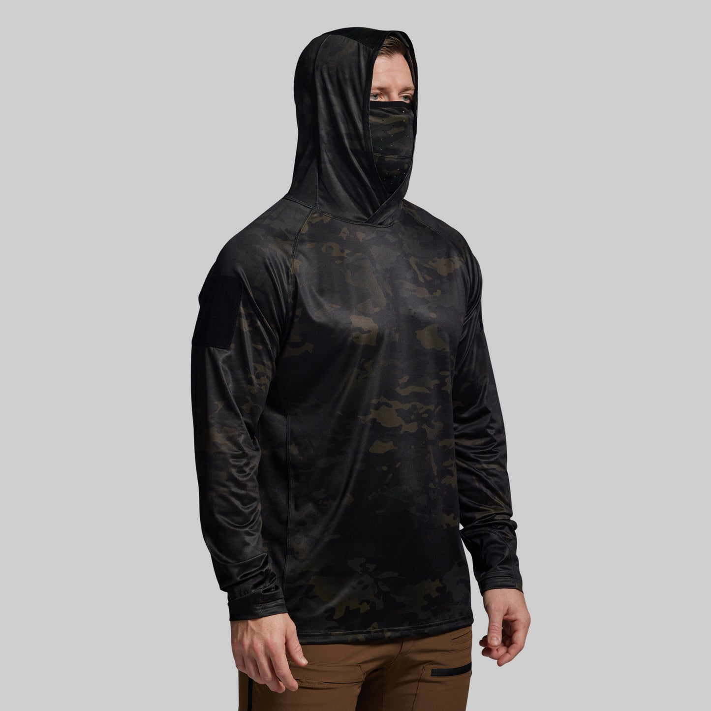 Person wearing a black hooded shirt with built-in face mask and camouflage pattern on a gray background