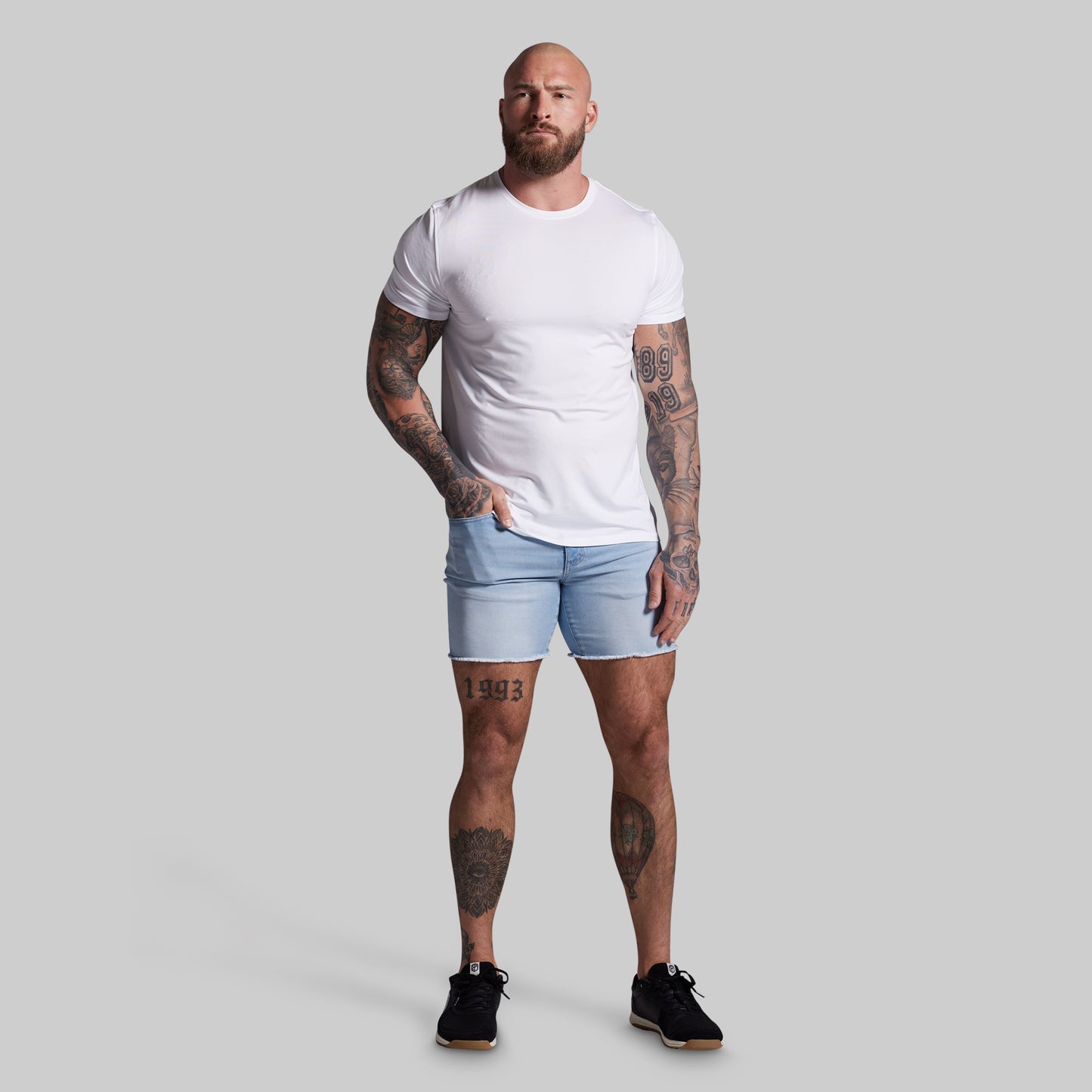 Man wearing a white t-shirt and light blue shorts on a gray background