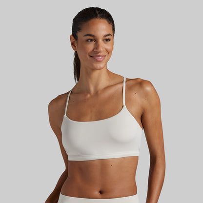 A woman modeling a white lounge bra against a solid gray studio background.