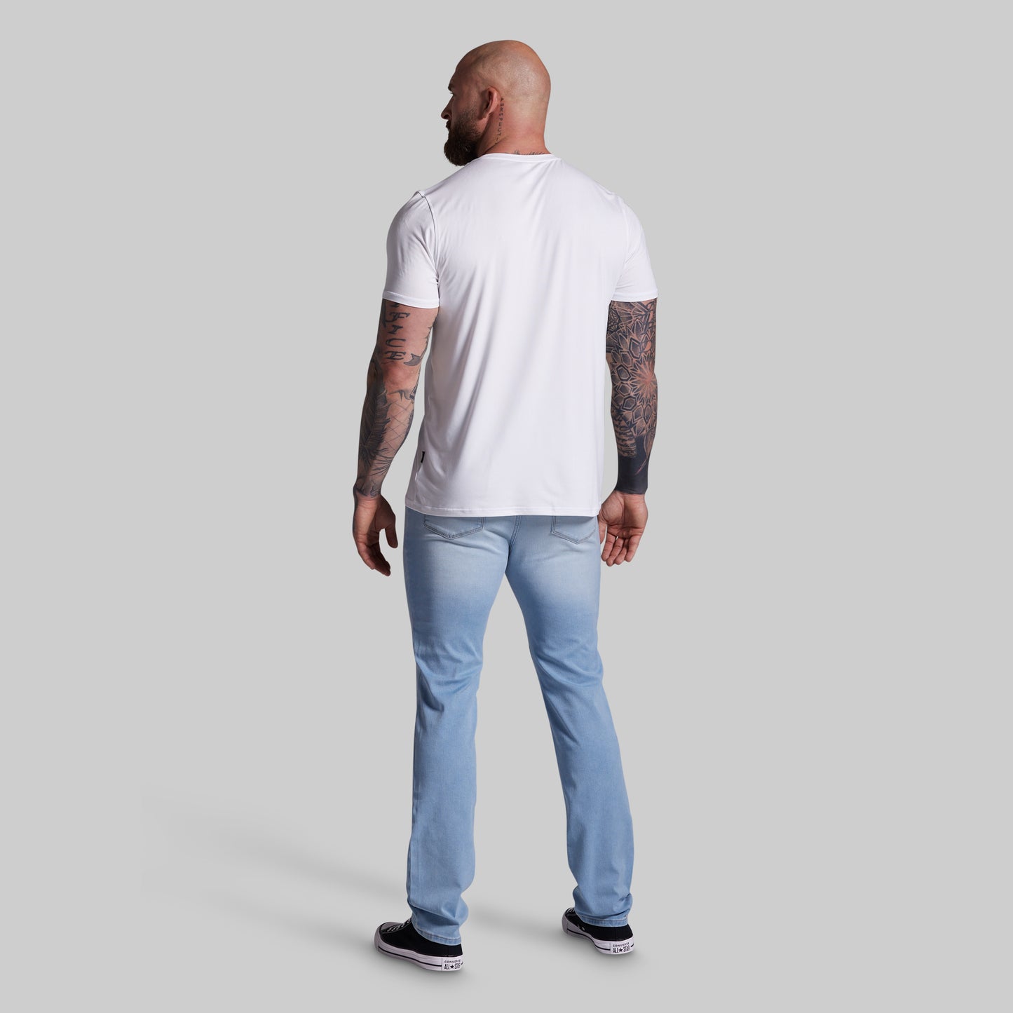 Man wearing a white t-shirt and light blue jeans on a gray background
