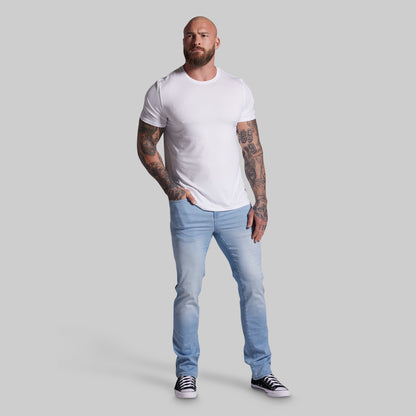 Man wearing a white t-shirt and light blue jeans on a gray background