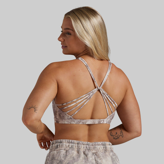 A woman shown from the back wearing a strappy sports bra and matching patterned sweatpants against a plain light gray studio background.