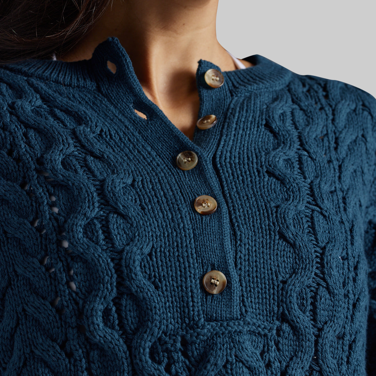 Close-up of a woman wearing a dark teal cable-knit sweater with a buttoned split neckline and brown buttons.