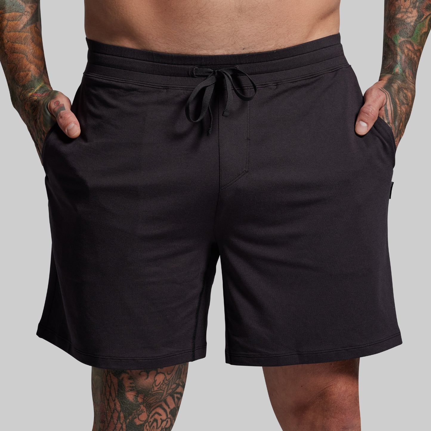 Black shorts worn by a person with tattoos on a gray background