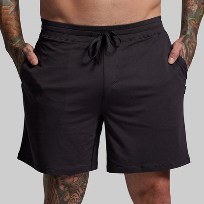 Black shorts worn by a person with tattoos on a gray background