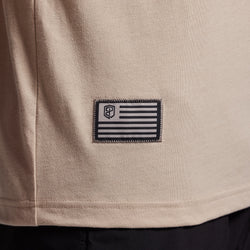 Close-up of a beige t-shirt with a black and gray flag patch.