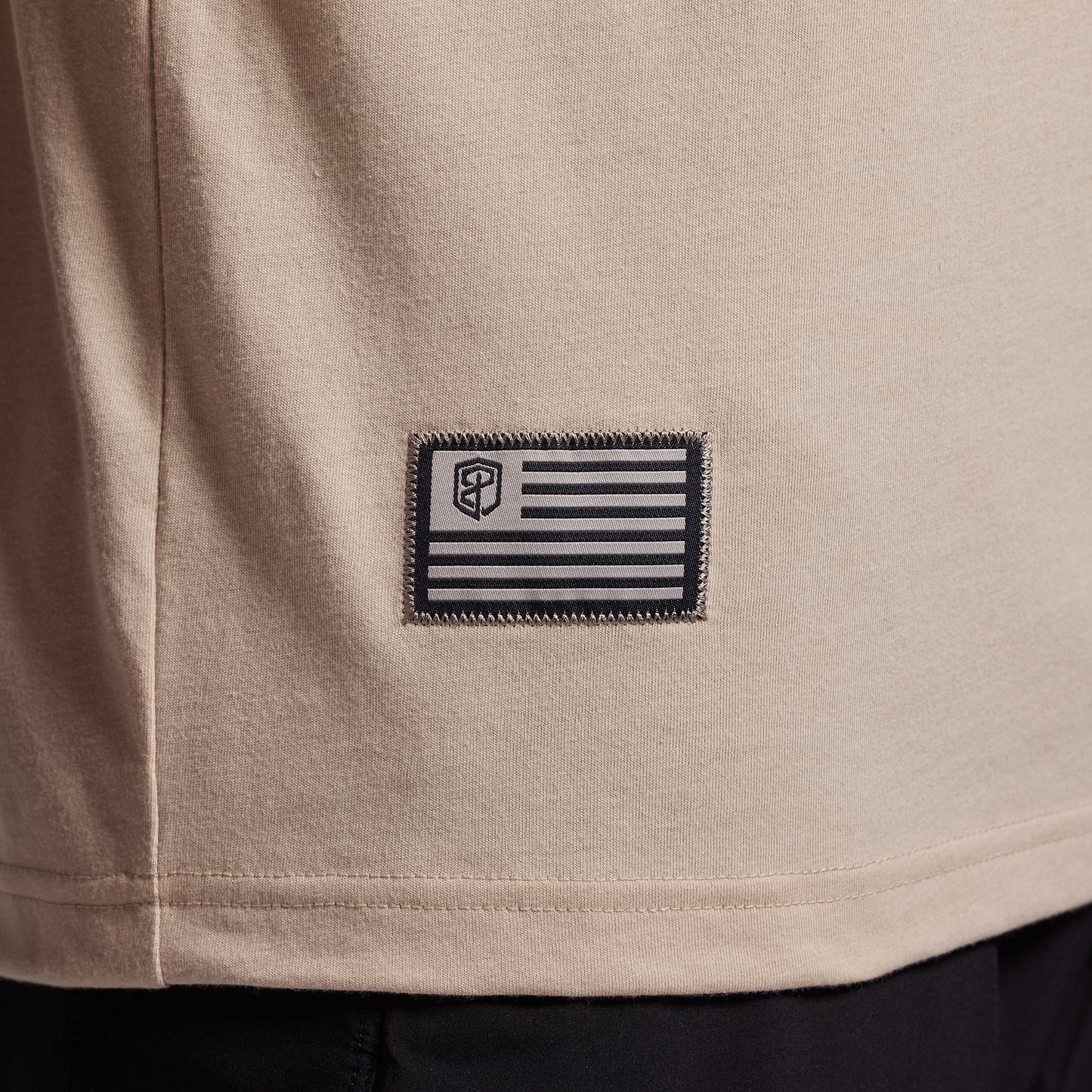 Close-up of a beige t-shirt with a black and gray flag patch.
