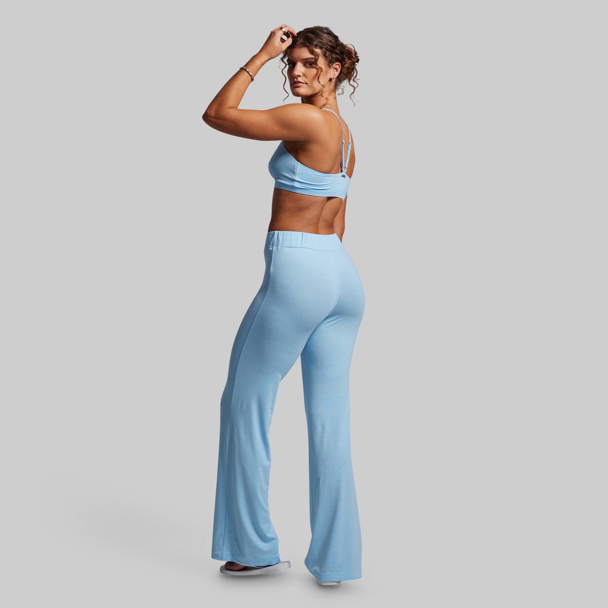 Woman wearing a light blue sports bra and high-waisted wide-leg pants on a gray background