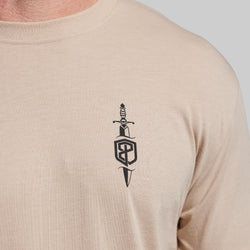 Beige t-shirt with a black dagger and shield logo on the chest.