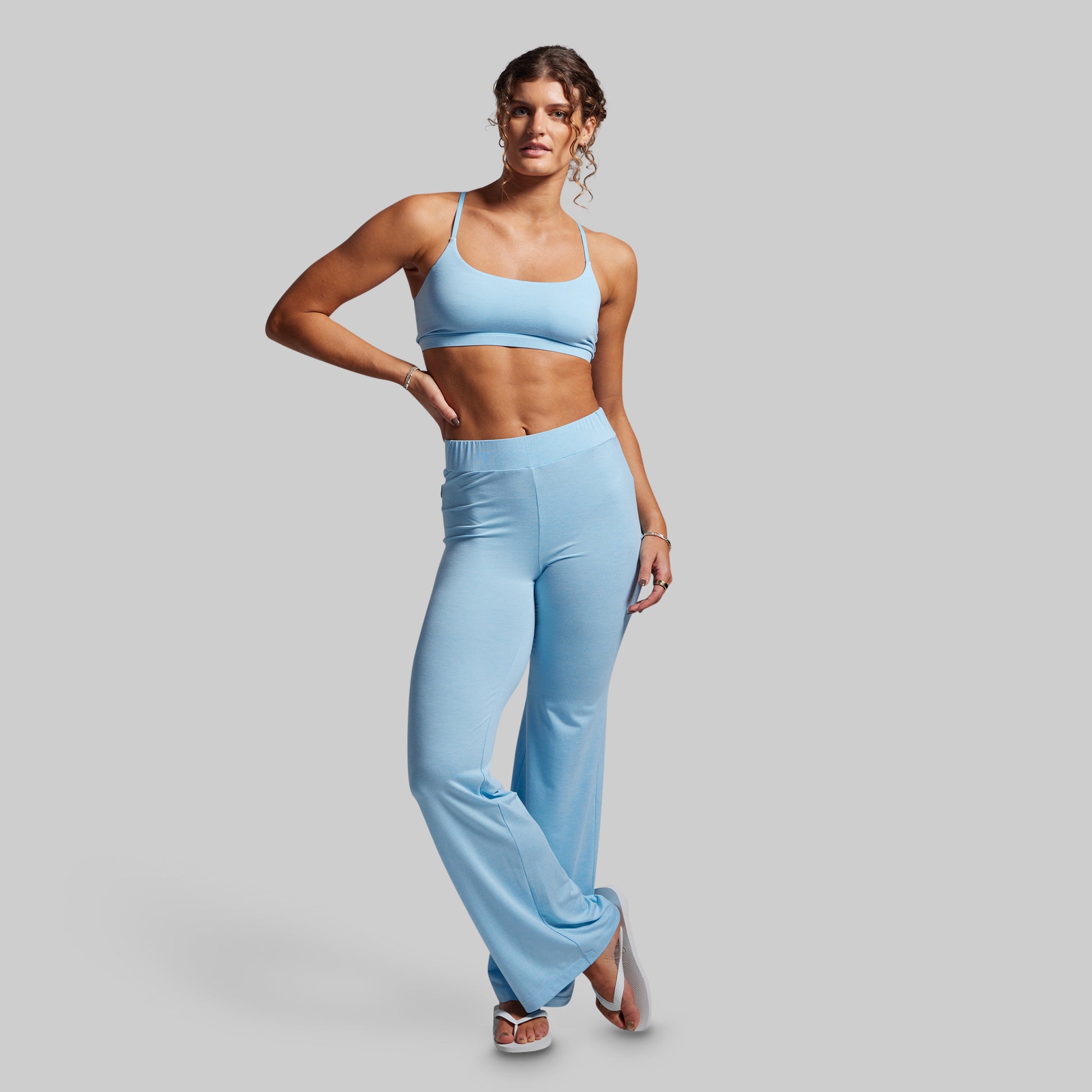 Woman wearing a light blue sports bra and high-waisted wide-leg pants on a gray background