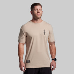 Man wearing a beige t-shirt with a logo on a plain background