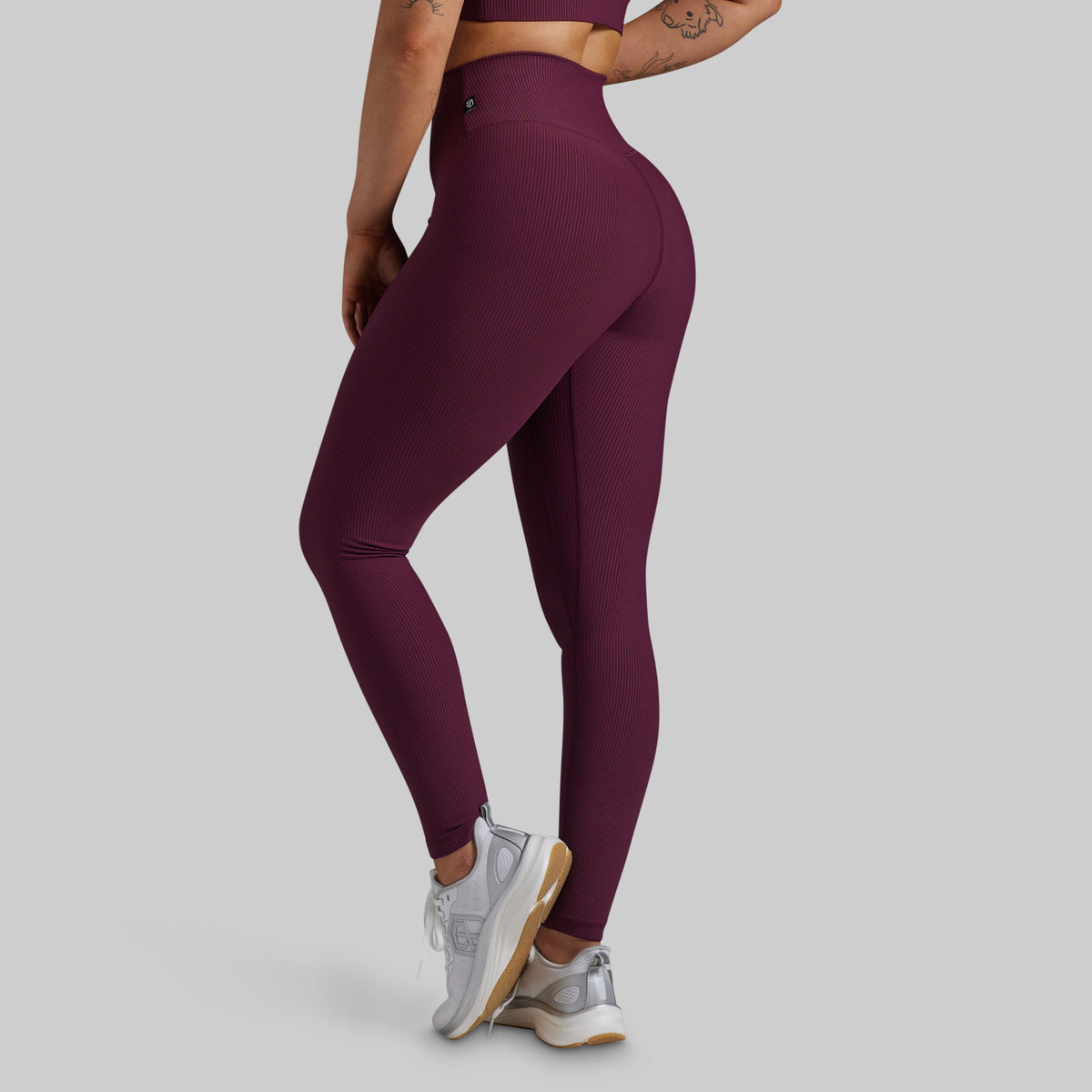 A model wearing high-waisted, form-fitting leggings in a deep plum purple color, shown from a side-rear angle against a solid light gray background.