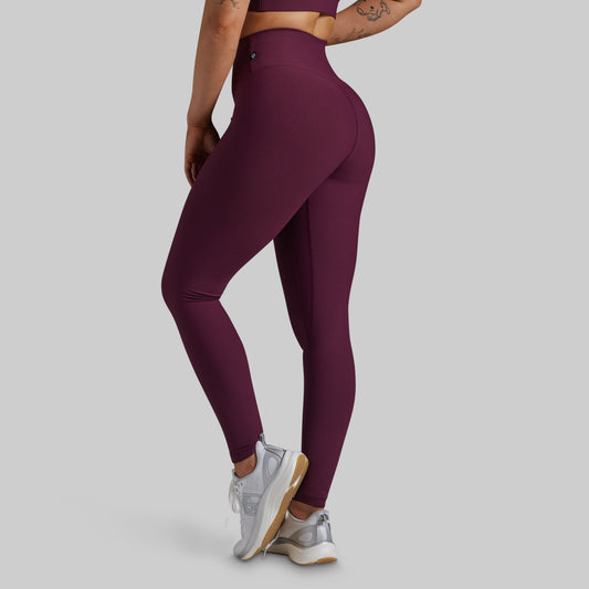 A model wearing high-waisted, form-fitting leggings in a deep plum purple color, shown from a side-rear angle against a solid light gray background.