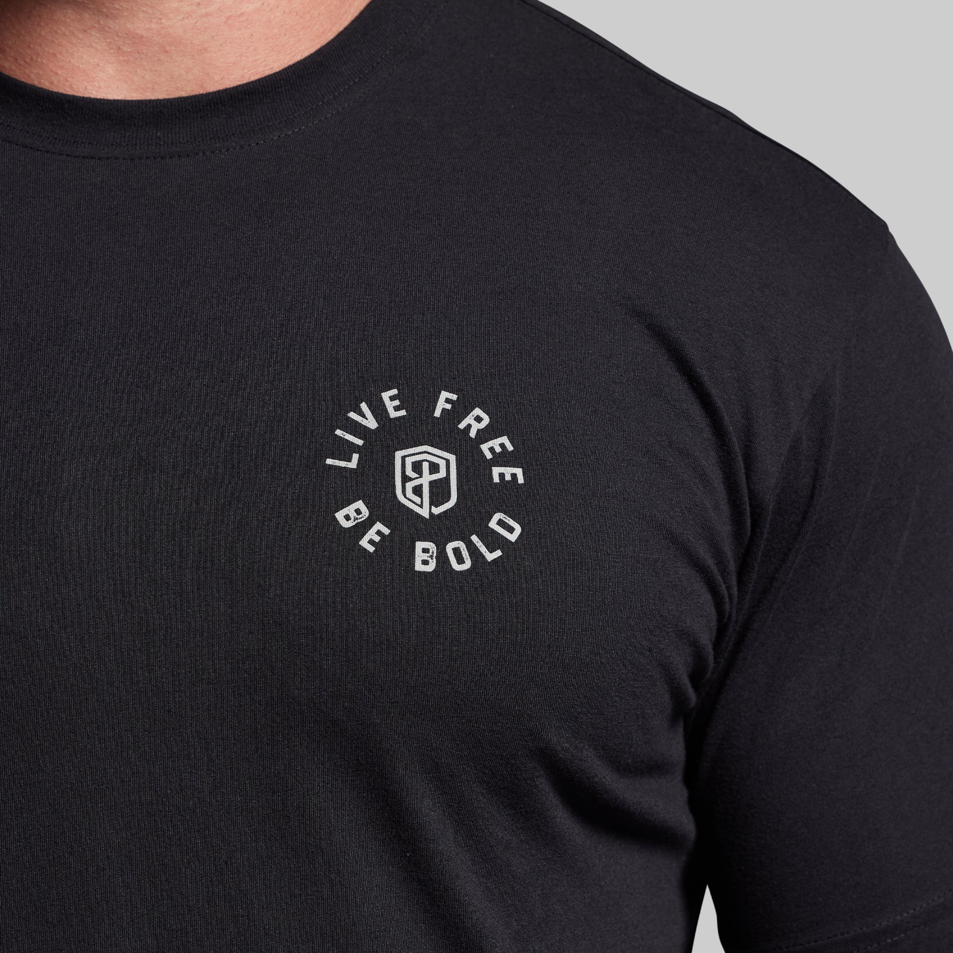 Black t-shirt with 'Live Free Be Bold' text on a gray background