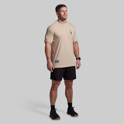 Man wearing a beige t-shirt and black shorts on a gray background