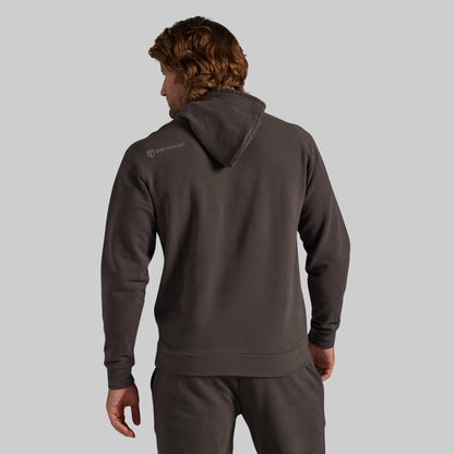A man shown from the back wearing a dark charcoal gray hoodie and matching sweatpants against a solid light gray background.