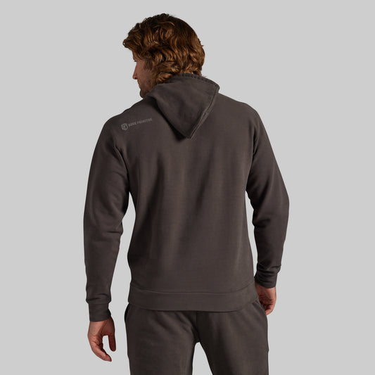 A man shown from the back wearing a dark charcoal gray hoodie and matching sweatpants against a solid light gray background.