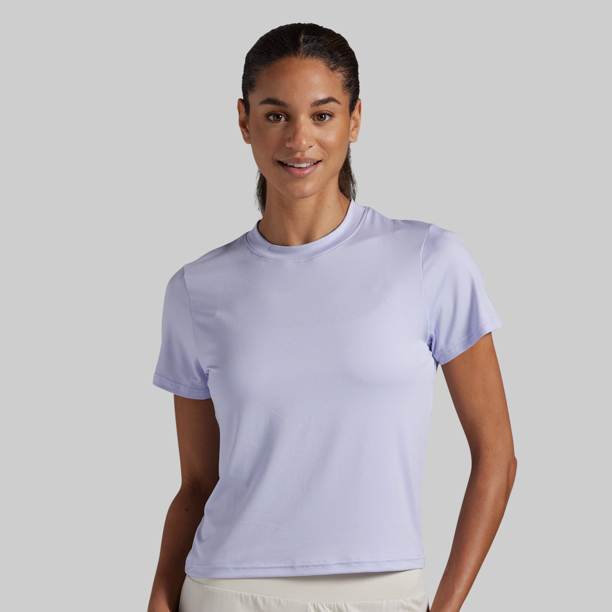 A woman modeling a light lavender short-sleeve crewneck athletic t-shirt against a solid light gray background.